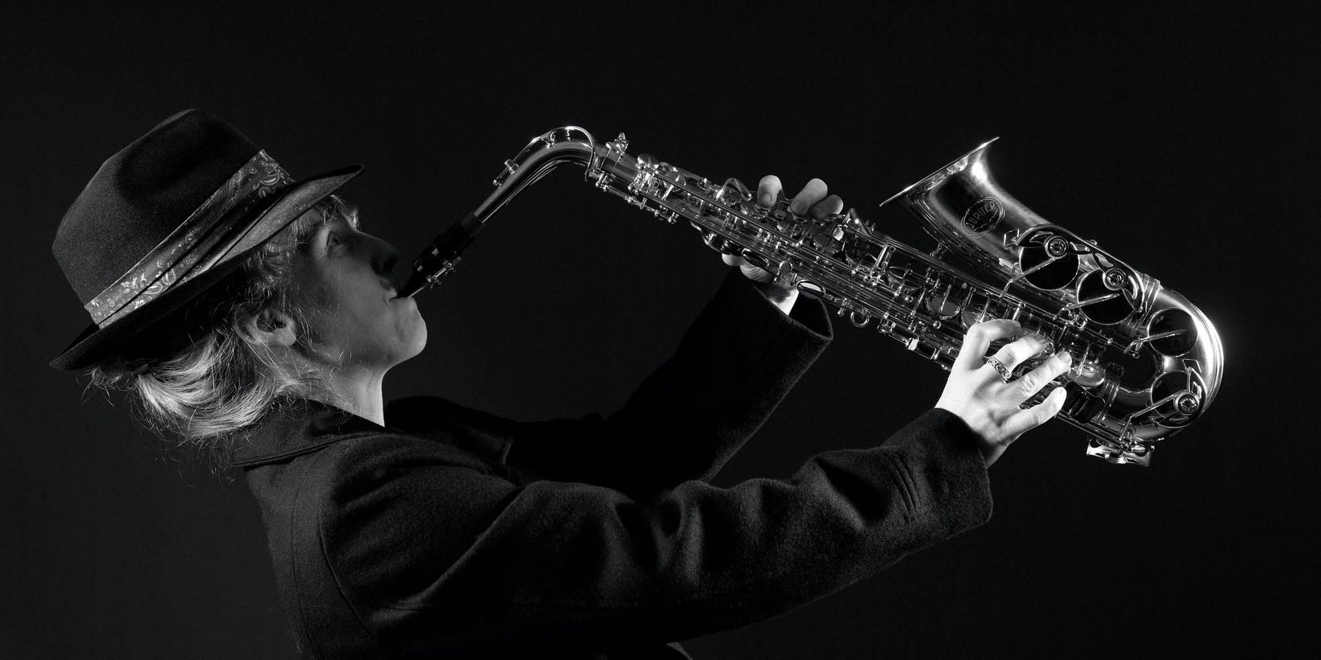Auf einem Schwarzweißfoto spielt ein Mann mit Hut Saxophon.