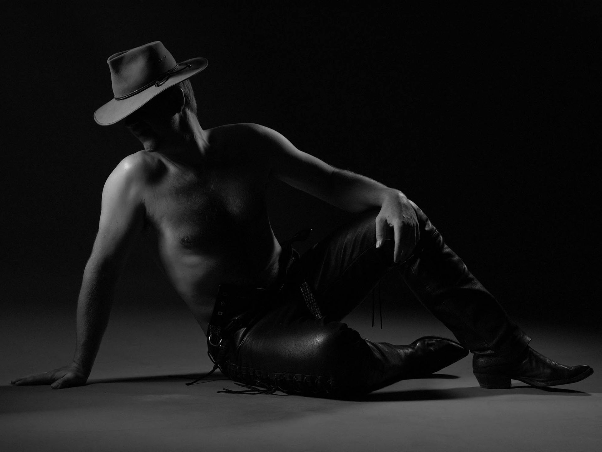 Ein Mann ohne Hemd, mit Cowboyhut und Lederhose liegt auf dem Boden.