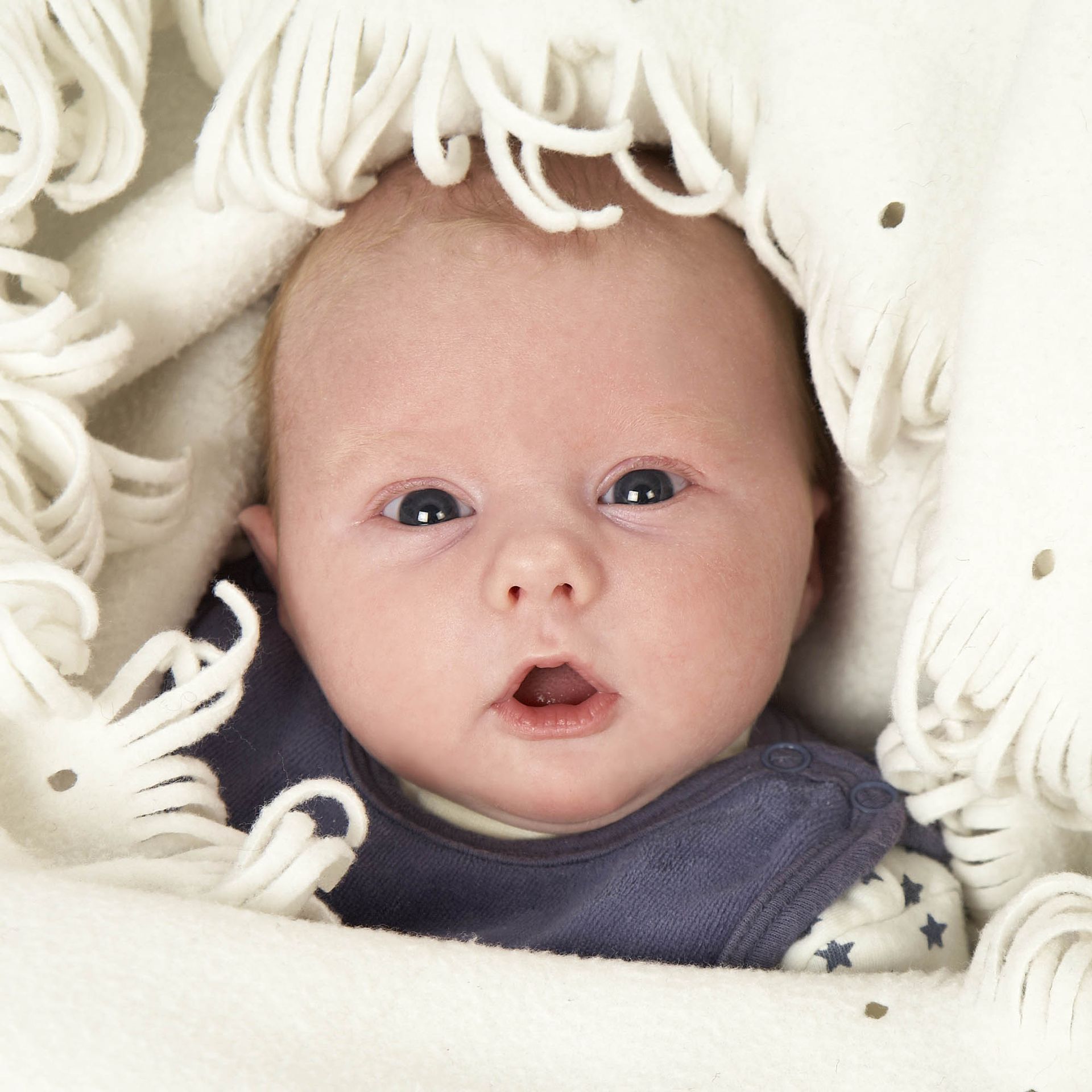 Ein Baby ist in eine weiße Decke gehüllt und schaut in die Kamera