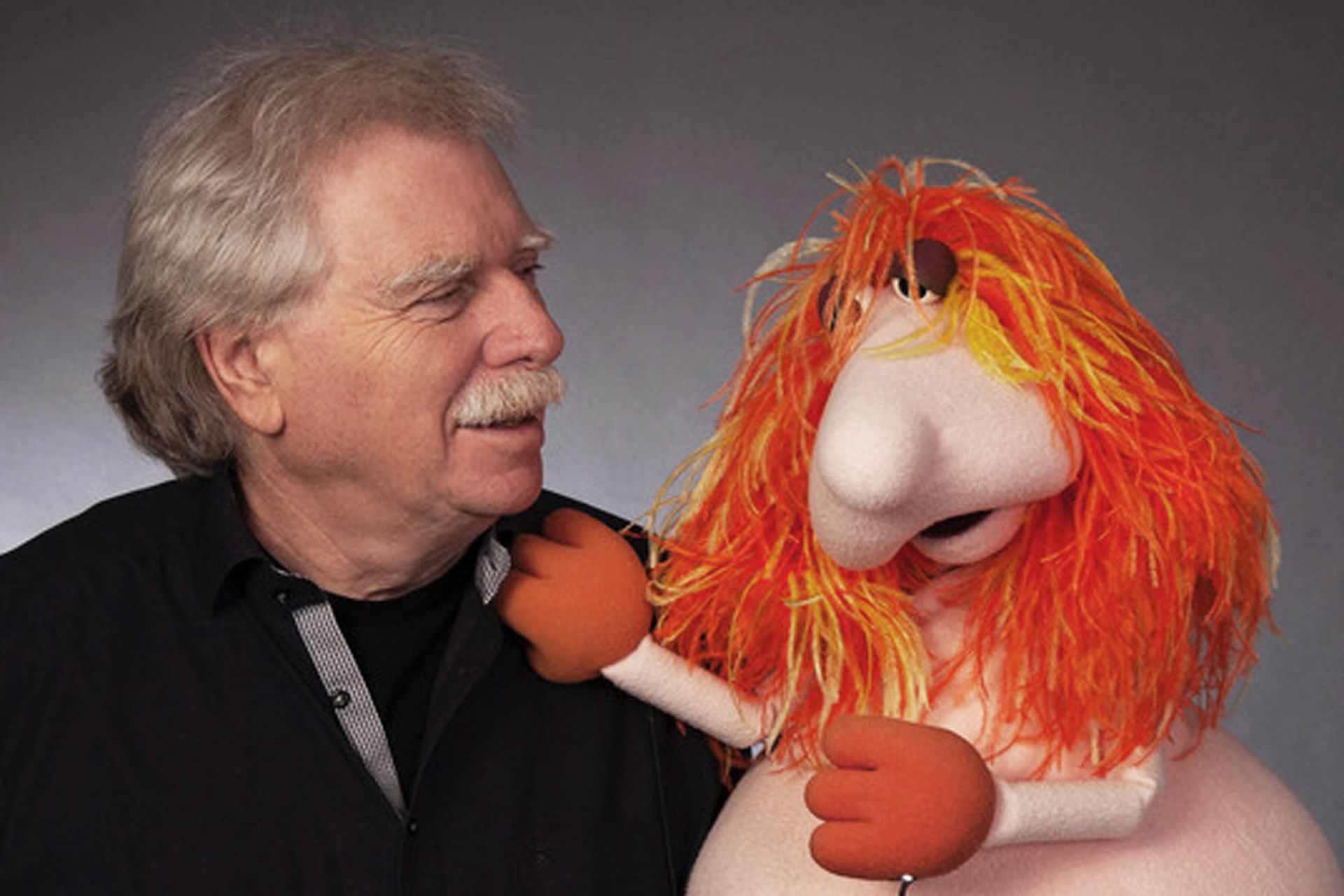 Ein Mann steht neben einer Puppe mit orangefarbenen Haaren.