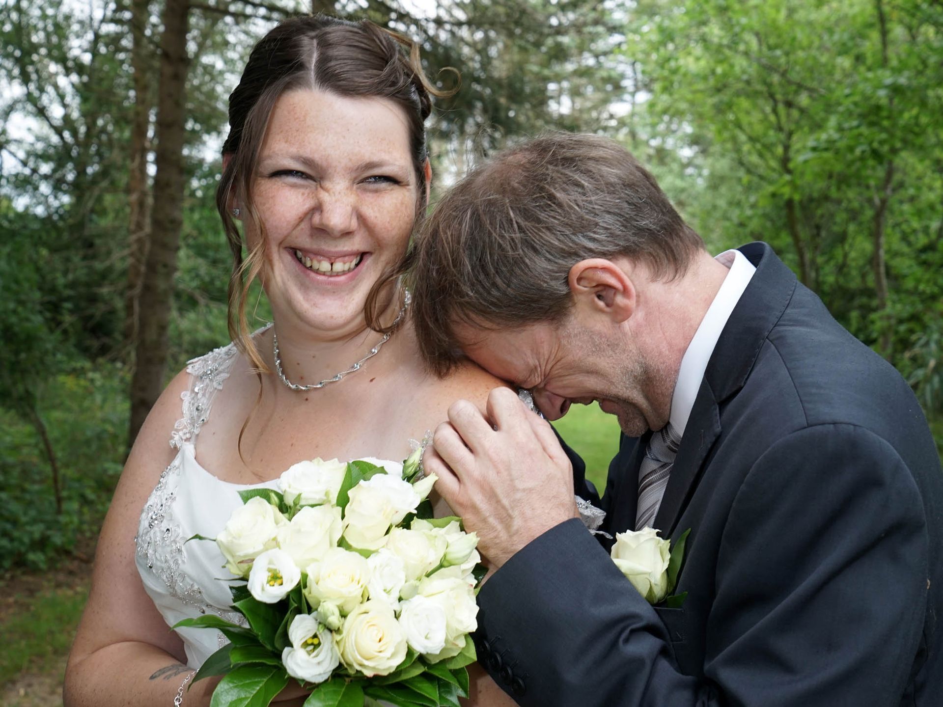 Braut und Bräutigam posieren für ein Foto und die Braut hält einen Strauß weißer Rosen.
