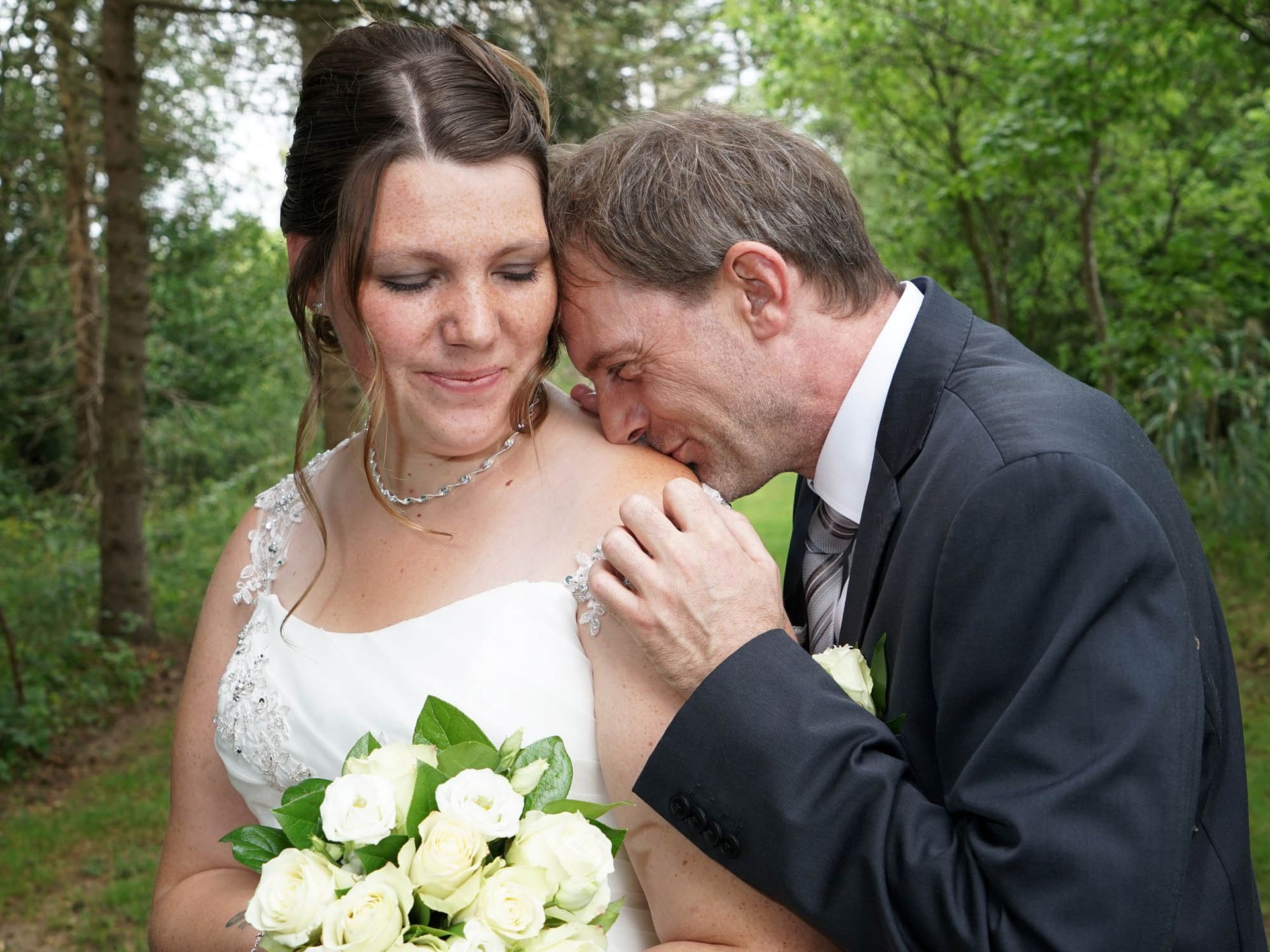 Ein Mann küsst die Schulter einer Frau im Brautkleid.