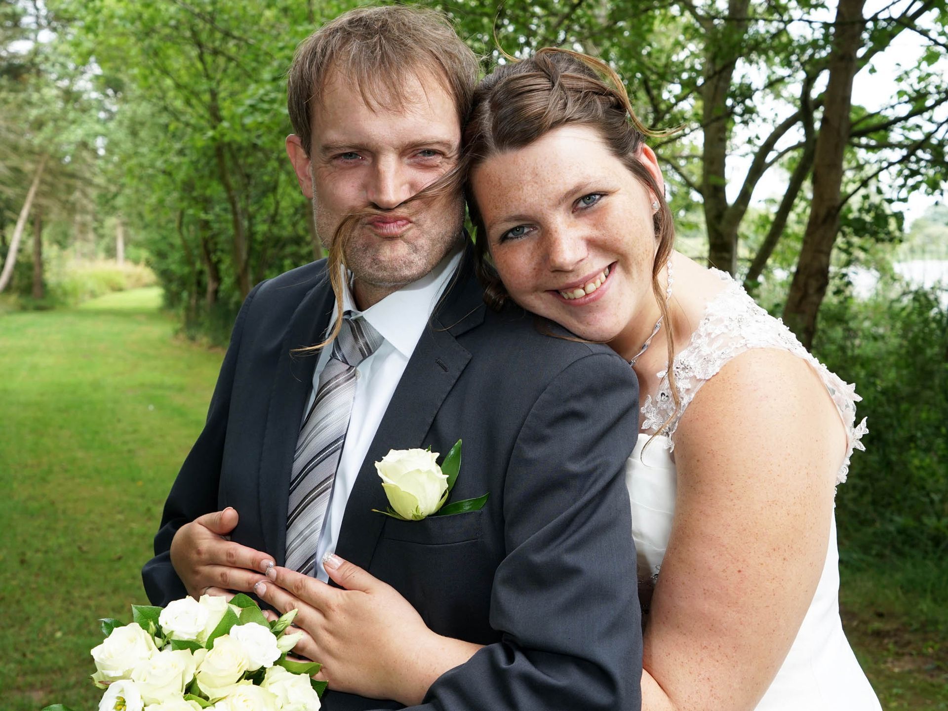 Eine Braut und ein Bräutigam posieren für ein Foto und die Braut hat eine Blume in der Nase.