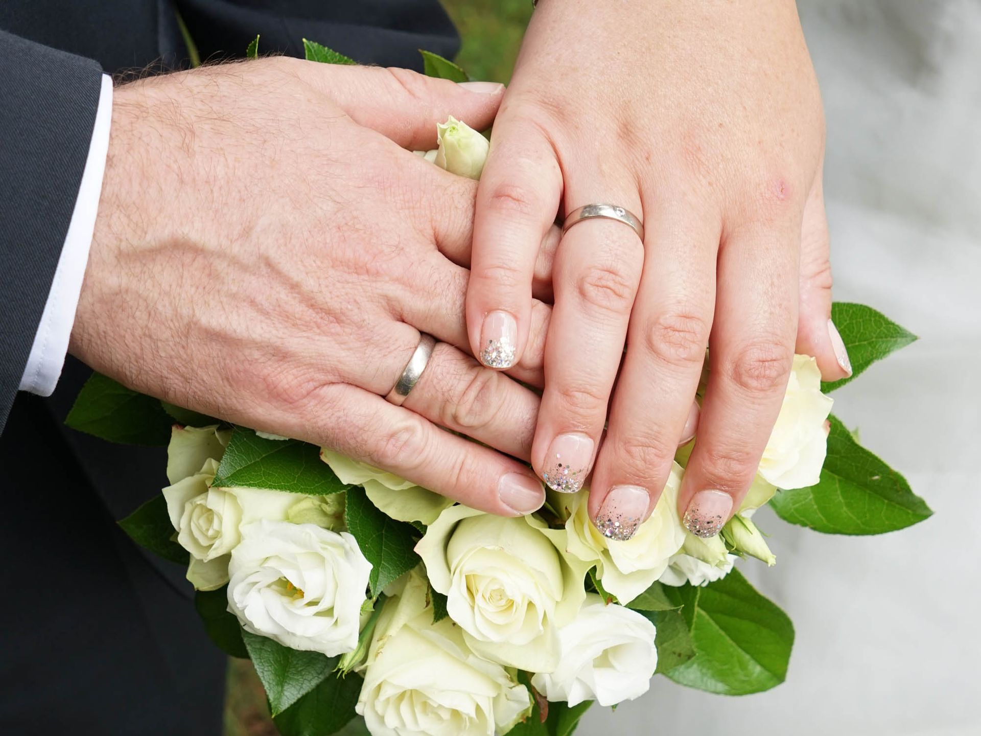 Eine Braut und ein Bräutigam halten einen Strauß weißer Rosen und tragen ihre Eheringe an den Fingern.