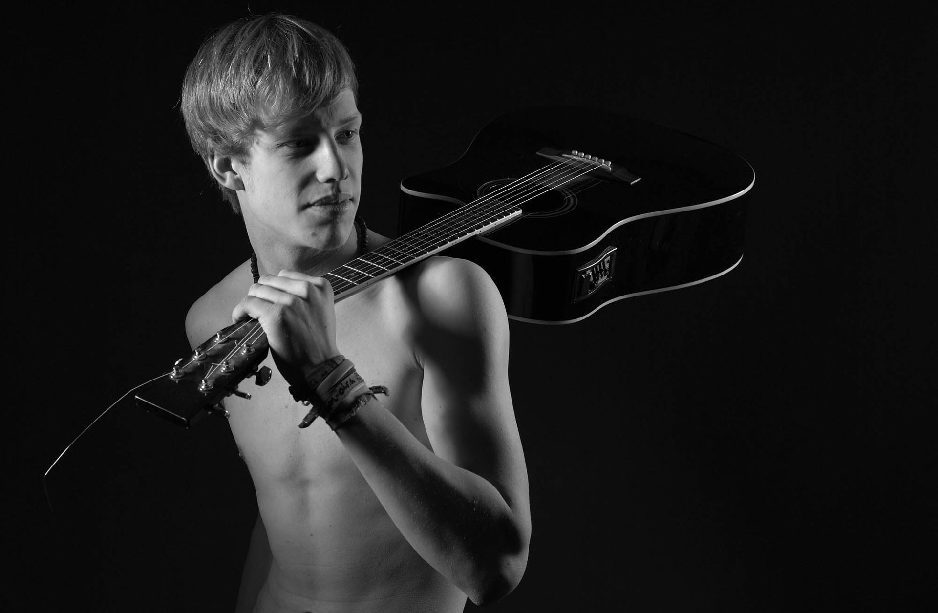 Ein Mann ohne Hemd hält eine Gitarre über seiner Schulter.