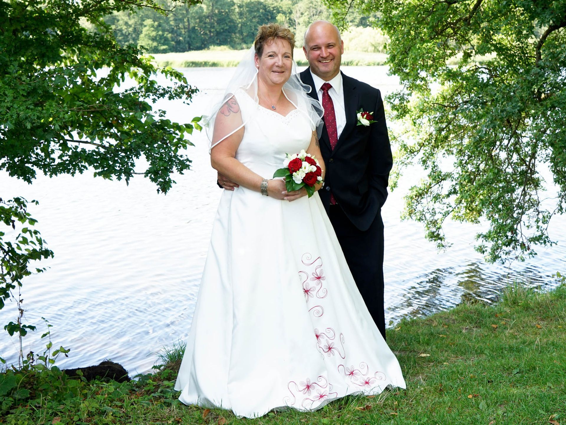 Eine Braut und ein Bräutigam posieren für ein Foto vor einem See.