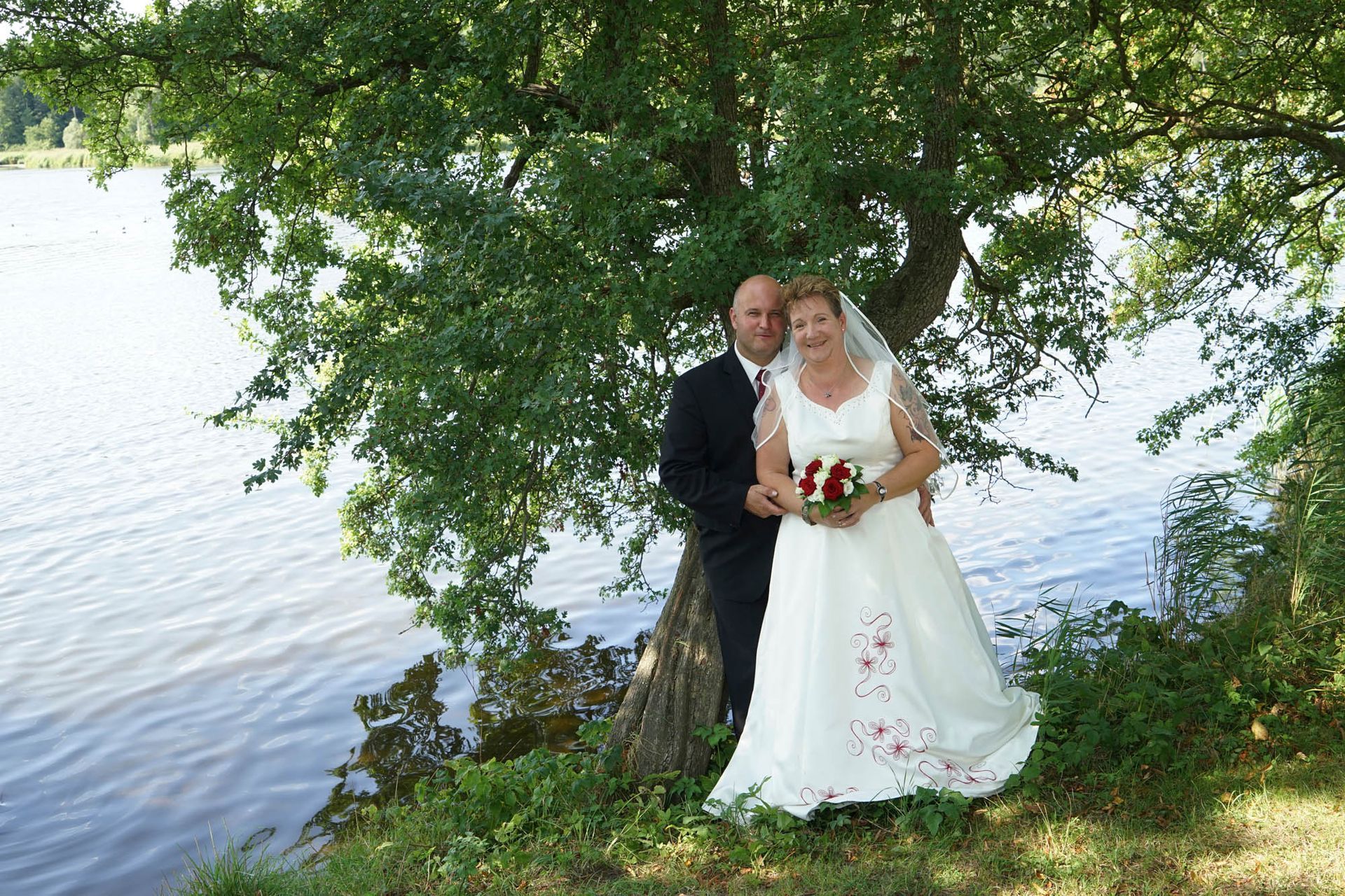 Braut und Bräutigam posieren unter einem Baum in der Nähe eines Gewässers
