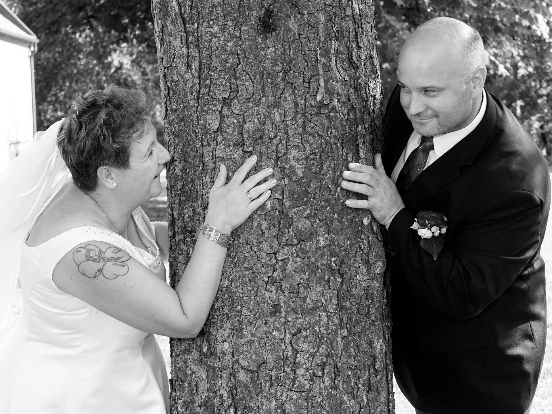 Auf einem Schwarzweißfoto umarmen eine Braut und ein Bräutigam einen Baum.