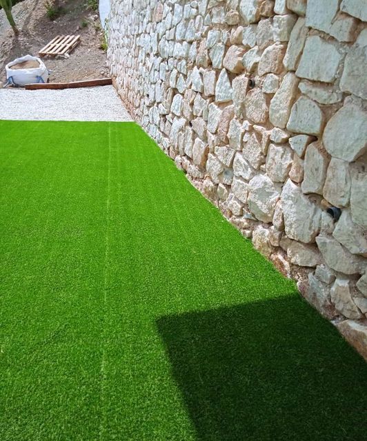 Hay un muro de piedra detrás de un exuberante césped verde.
