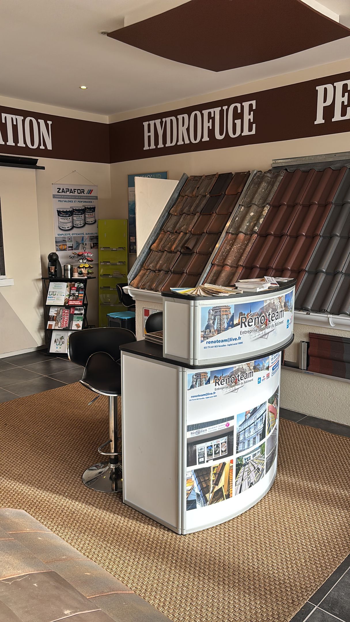Présentoir avec brochures et petit support dans un hall intérieur recouvert de moquette.