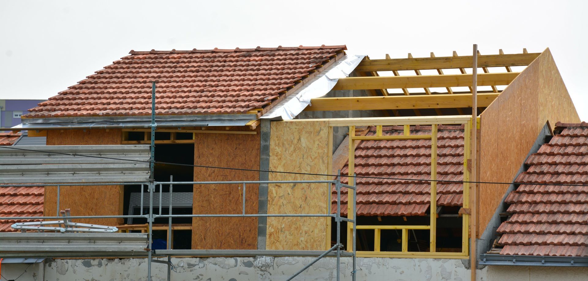 Maison en construction avec murs en briques, toit de tuiles rouges et charpente apparente en bois.