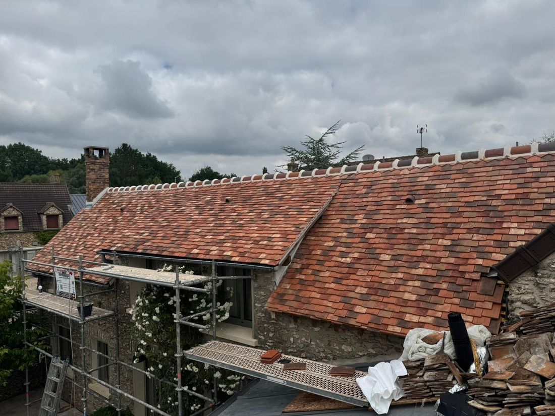 Des échafaudages contre un bâtiment en pierre au toit de tuiles multicolores fraîchement posé, sous un ciel nuageux.