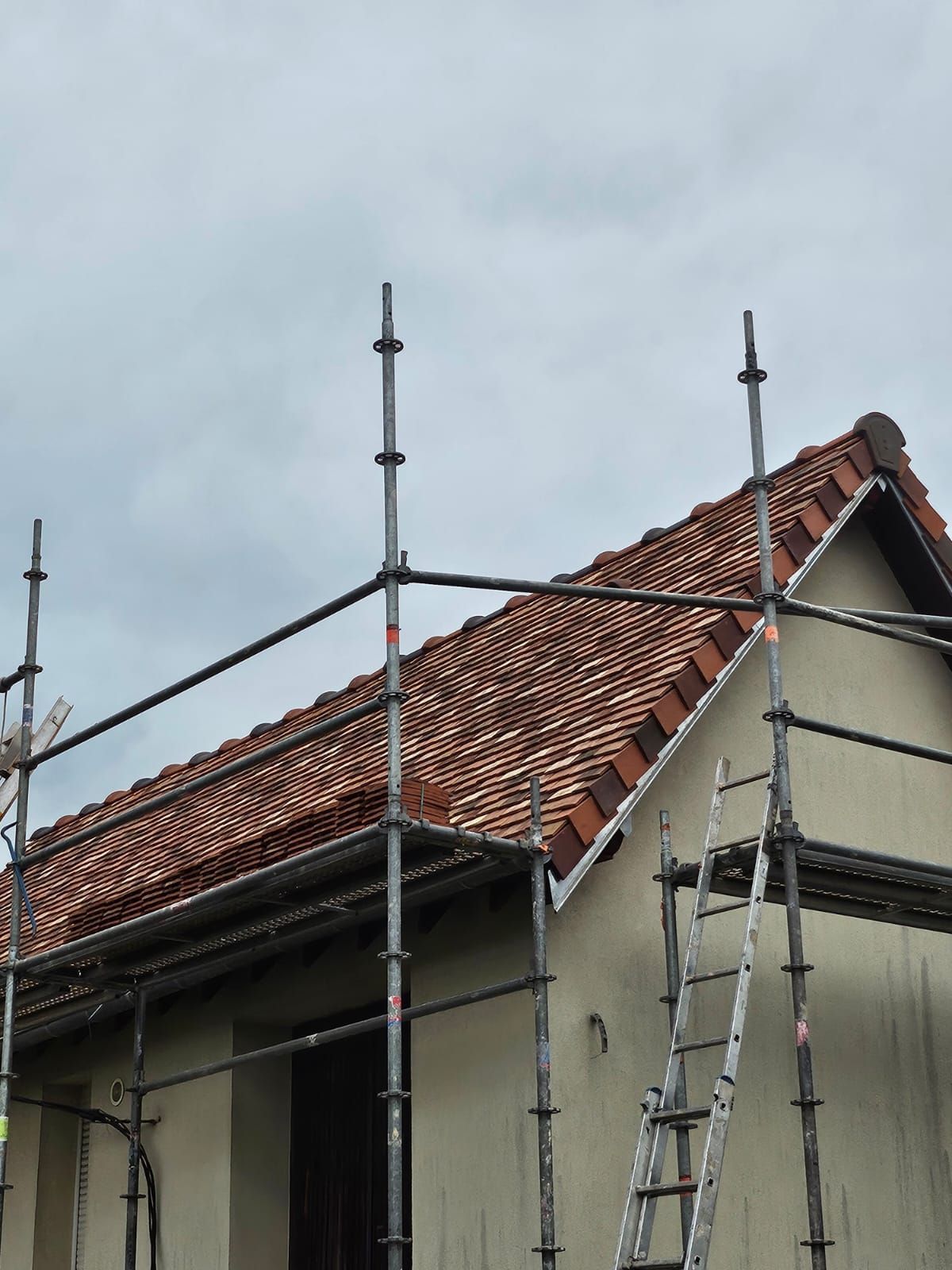 Échafaudages autour d'une maison en rénovation avec un toit de tuiles rouges