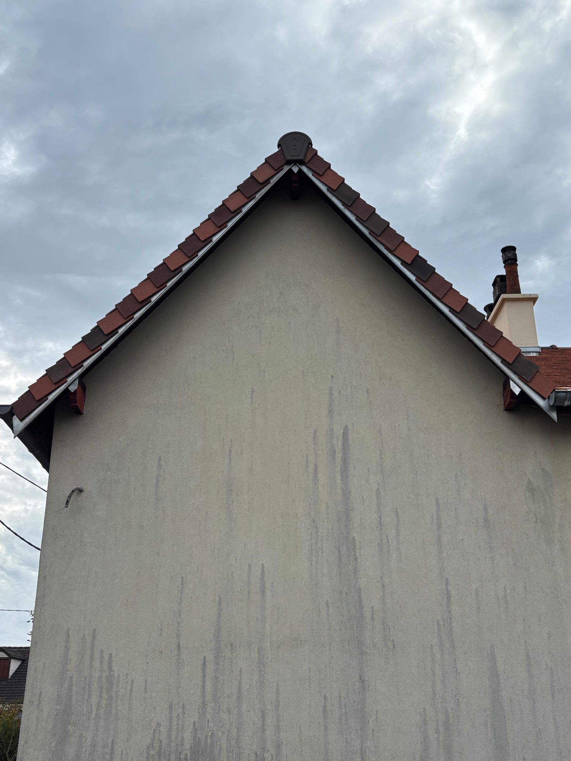 Vue de face du pignon d'une maison au toit de tuiles rouges sur fond de ciel nuageux