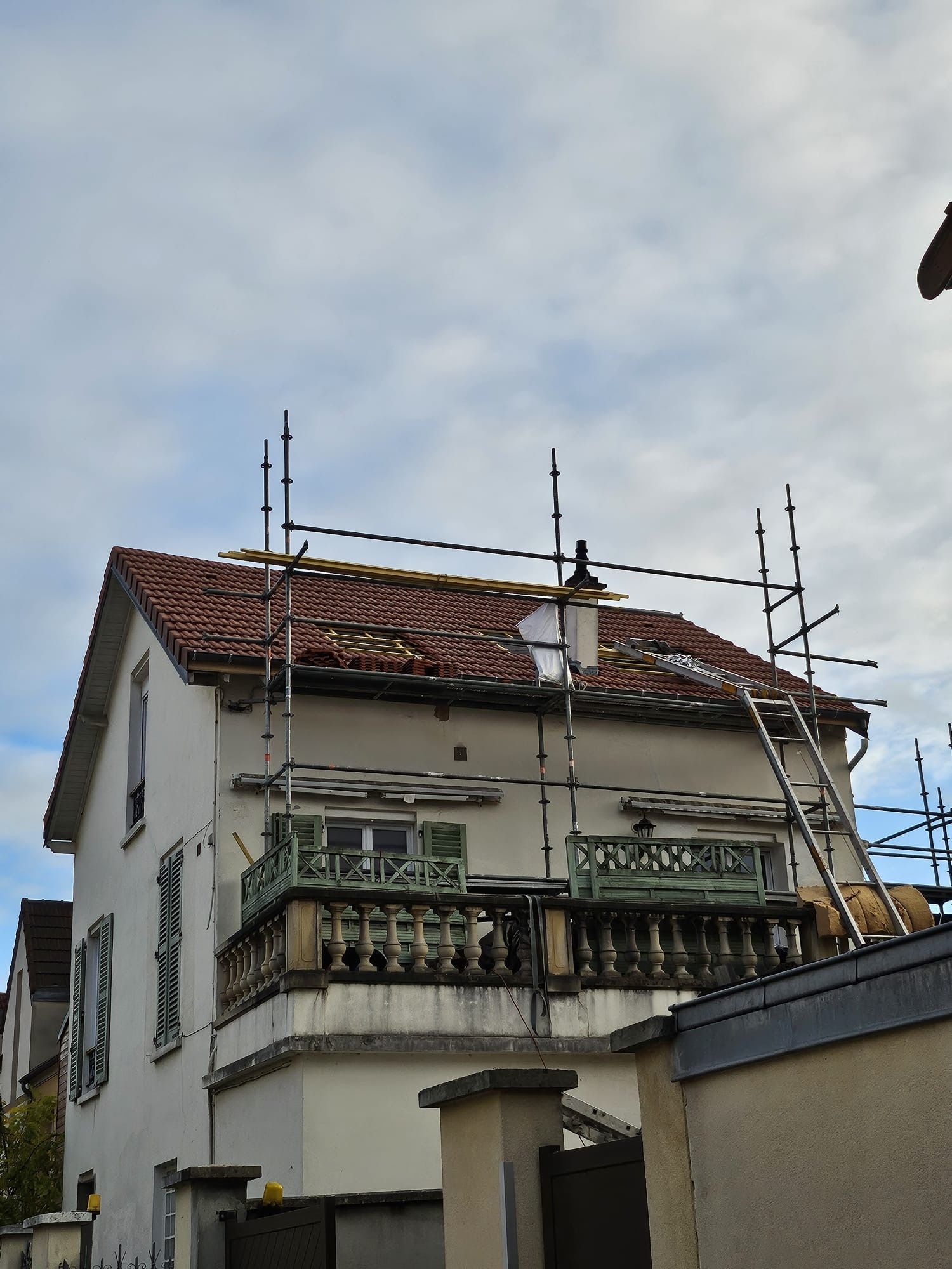 Vieille maison blanche au toit de tuiles rouges sous des échafaudages, vue d'en bas sur fond de ciel nuageux