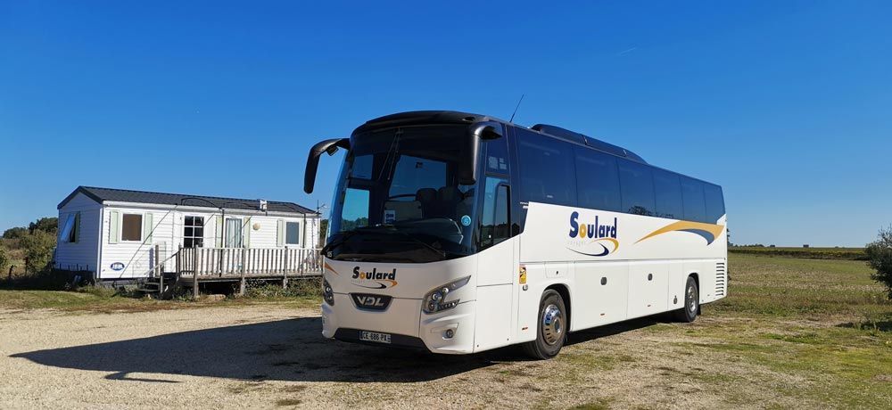 Un bus touristique blanc portant l'inscription « Souland » était garé sur un terrain vague à côté d'une caravane blanche, sous un ciel bleu azur.