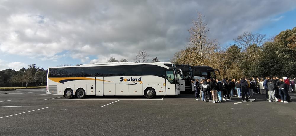 Deux autobus nolisés blancs, jaunes et noirs étaient stationnés sur un terrain vague, un groupe de personnes se tenant à proximité.