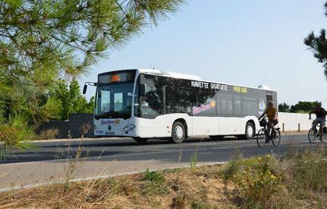 Un autobus blanc de transport en commun circule sur une route et dépasse deux cyclistes par une journée ensoleillée.