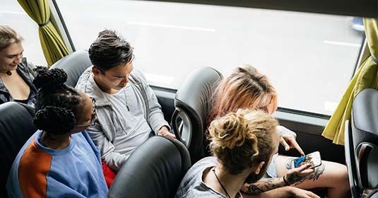 Un groupe de personnes assises ensemble dans un bus, regardant l'écran de leur téléphone.
