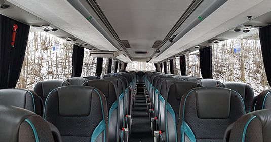 Vue intérieure d'un bus vide avec des sièges gris foncé et turquoise disposés en rangées face à l'avant, entourés de rideaux.