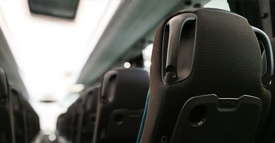 Gros plan sur l'arrière des sièges noirs d'un autobus de passagers, avec tablettes et poignées intégrées, dans une cabine faiblement éclairée.