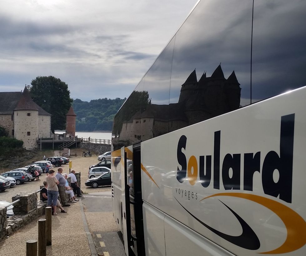 Un bus touristique Soulard garé à côté d'un parking près d'un château en pierre au bord de l'eau.