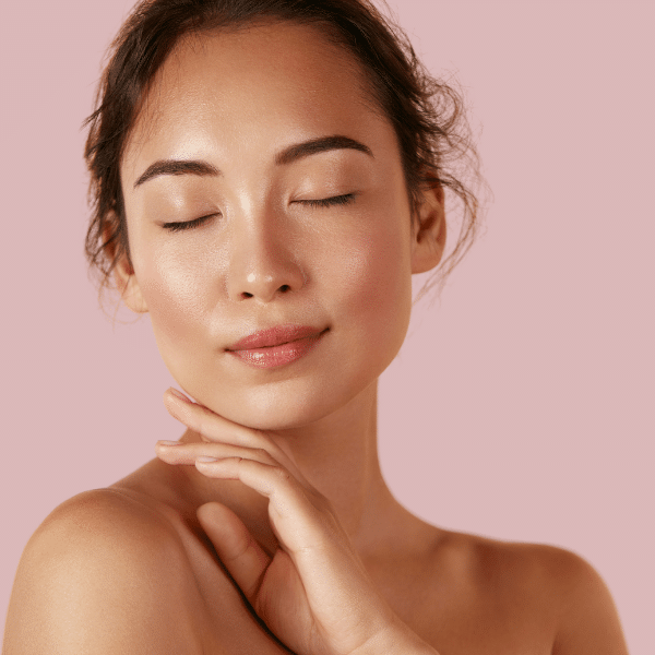 Portrait en gros plan d'une femme aux yeux fermés, touchant son épaule sur fond rose
