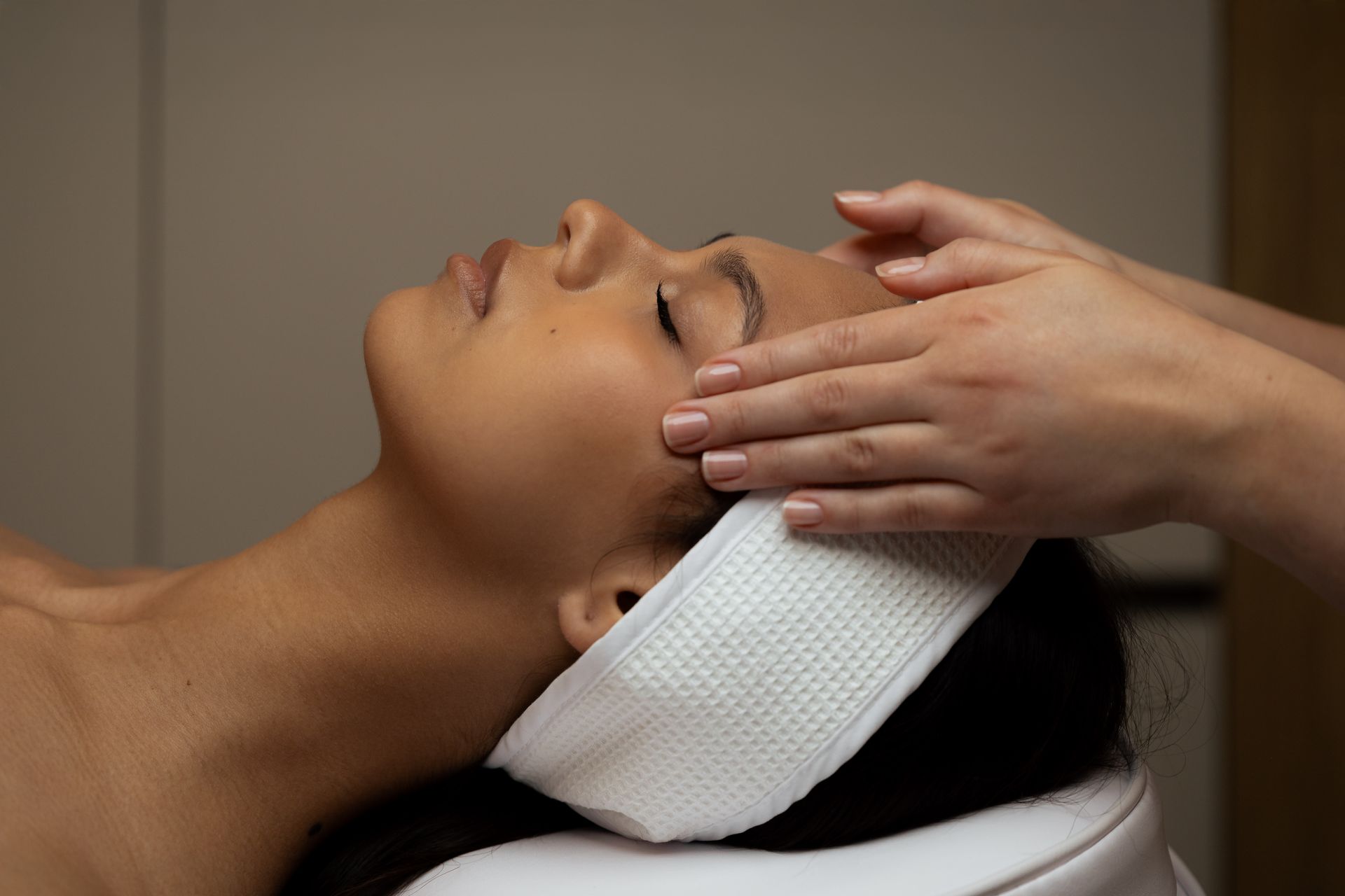Une femme enveloppée dans une serviette rose, souriant doucement tout en appliquant des soins du visage.