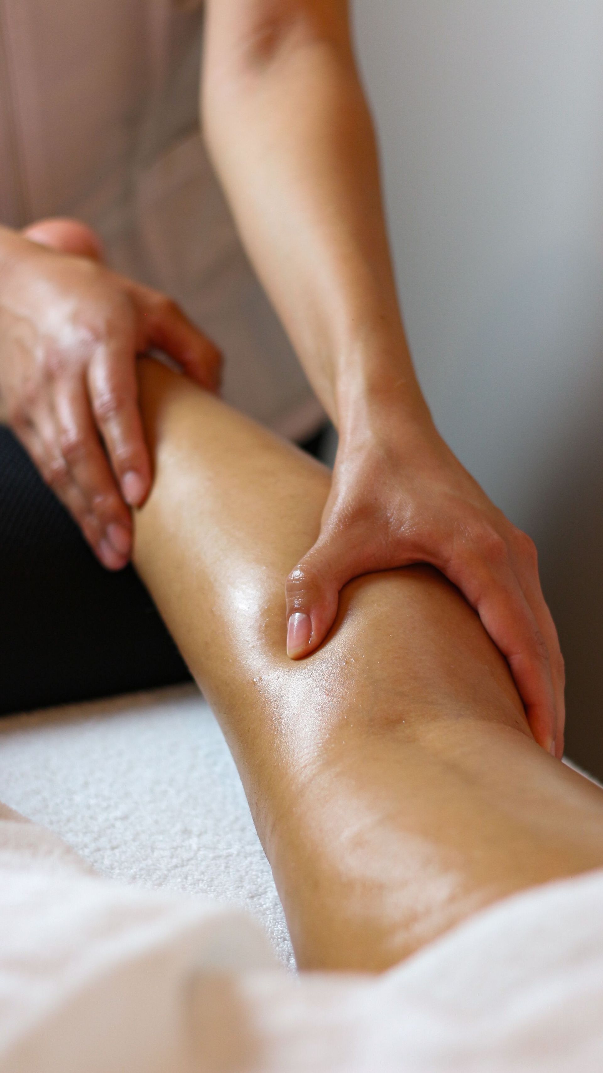 Une personne recevant un massage facial sur une table de soin, les yeux fermés, dans un spa.