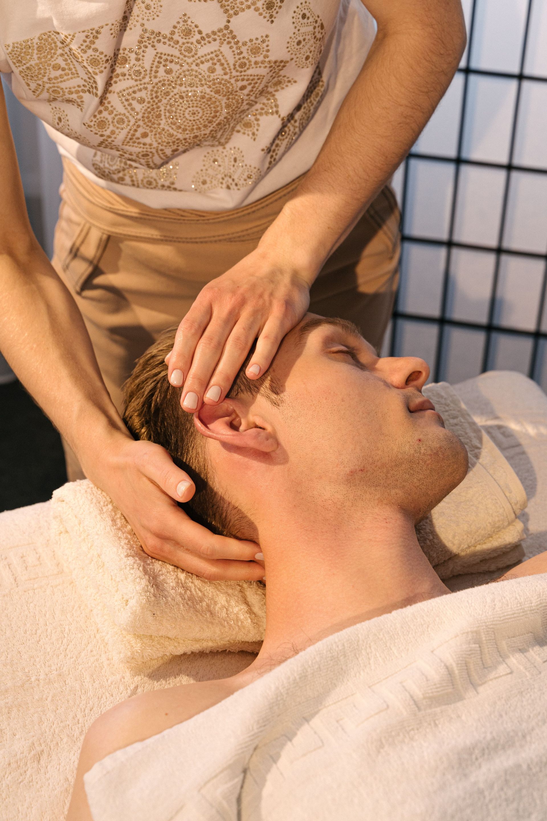 Une personne recevant un massage facial sur une table de soin, les yeux fermés, dans un spa.