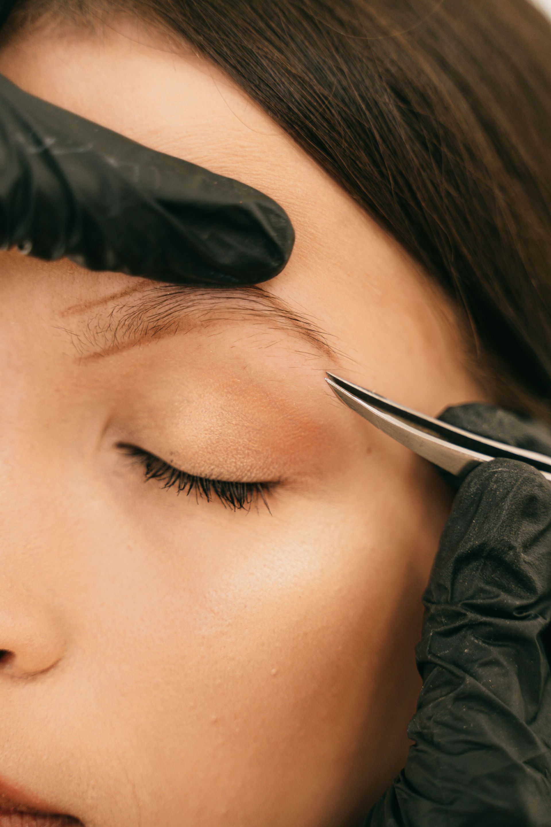 Gros plan sur l'épilation des sourcils à la pince à épiler par une main gantée