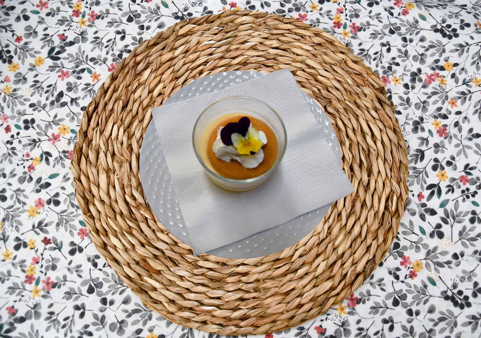 Postre en copa con crema, decoración de flores, sobre mantel tejido, mantel floral.