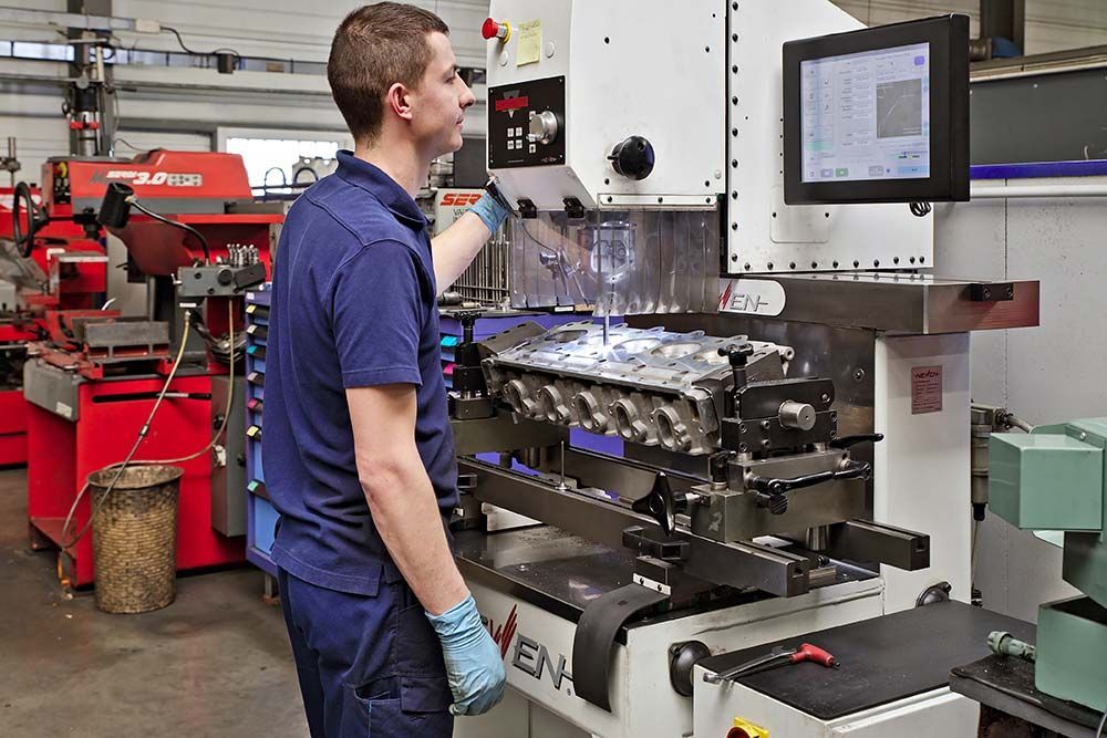 Technicien utilisant une machine à un poste de travail d'atelier avec un écran et des pièces de moteur