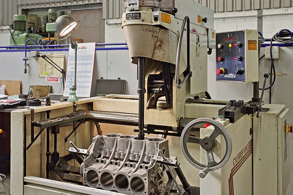 Atelier d'usinage industriel avec un gros bloc-moteur sur un établi et un panneau de commande en arrière-plan