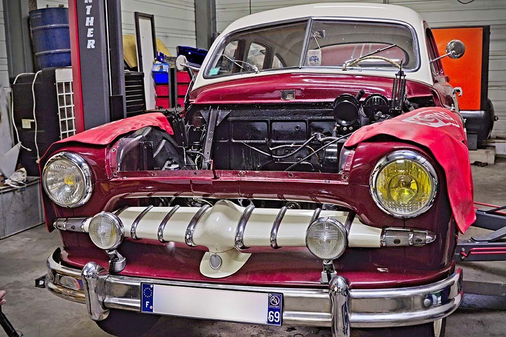 Voiture classique rouge vintage, capot ouvert, montrant la calandre avant dans un atelier de garage