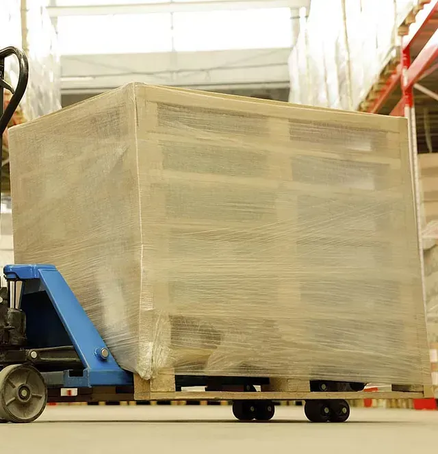 Una transpaleta transporta una caja grande envuelta en plástico en un almacén.