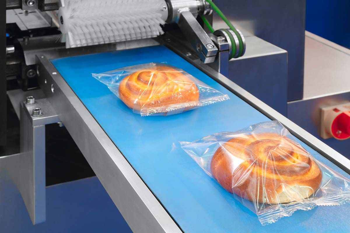 Dos rollos de pan están envueltos en plástico en una cinta transportadora.
