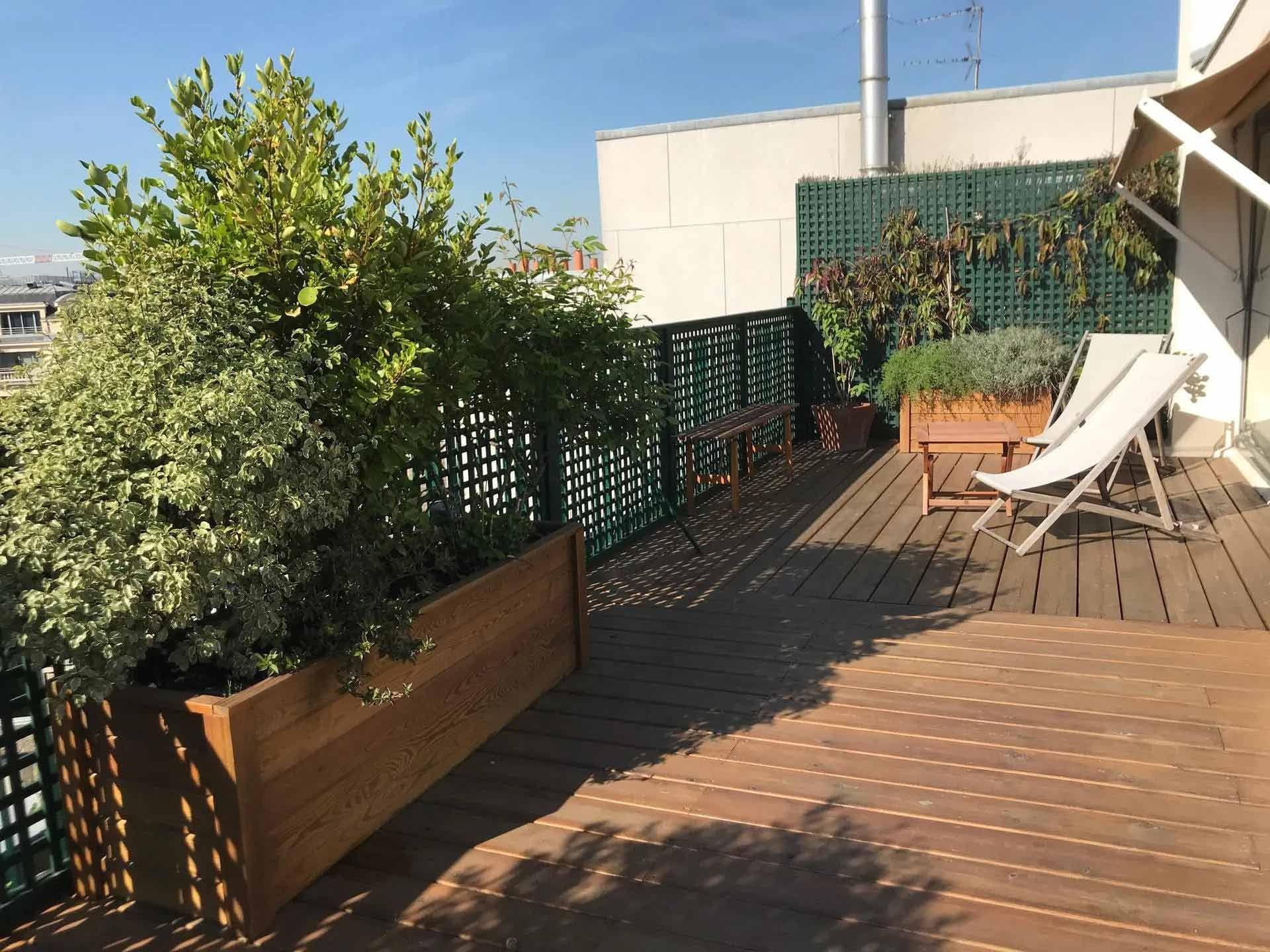 Grande terrasse en bois ensoleillée avec des claustras verts