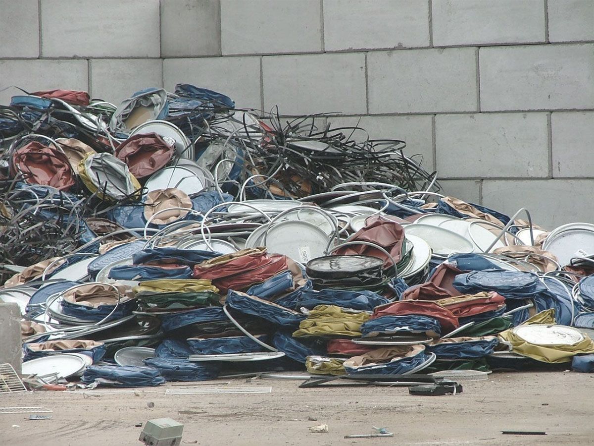 Un tas de chaises et de tables en métal et en tissu, mises au rebut, est adossé à un mur en béton gris.