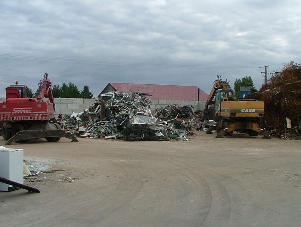 Centre de recyclage des métaux avec des tas de ferraille et deux excavatrices. Ciel nuageux.