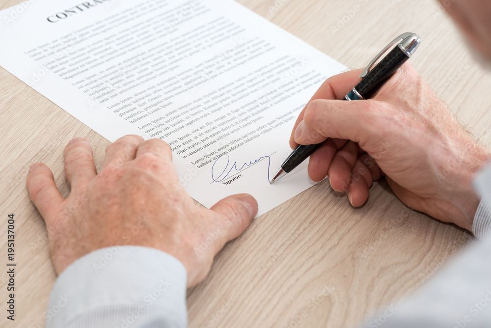 Une personne signe un contrat avec un stylo sur une table en bois.