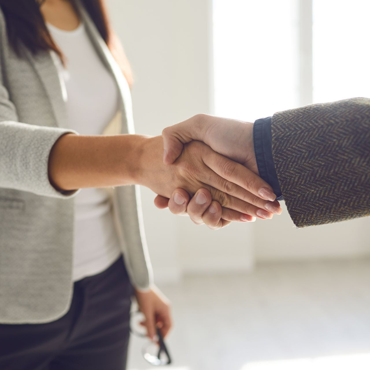 Deux personnes se serrent la main à l'intérieur, dans un contexte professionnel.