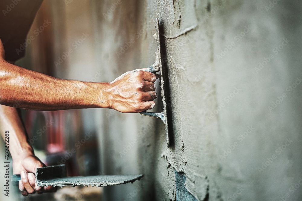 Un ouvrier utilise une truelle à main pour lisser le béton humide sur la surface d'un mur.