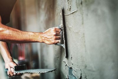 Un ouvrier utilise une truelle à main pour lisser le béton humide sur la surface d'un mur.