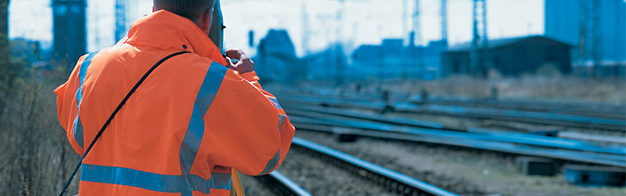 Ein Mann in einer orangefarbenen Jacke steht neben Bahngleisen.