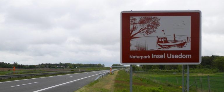 Ein rot-weißes Schild mit einem Boot darauf steht am Straßenrand.