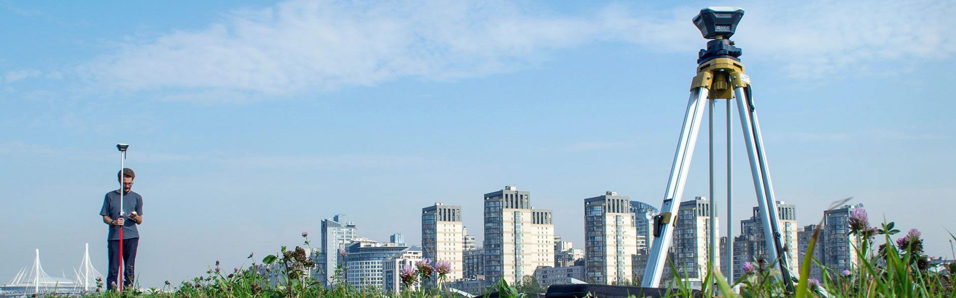 Ein Mann steht auf einem Feld mit der Skyline einer Stadt bei einer Vermessung.
