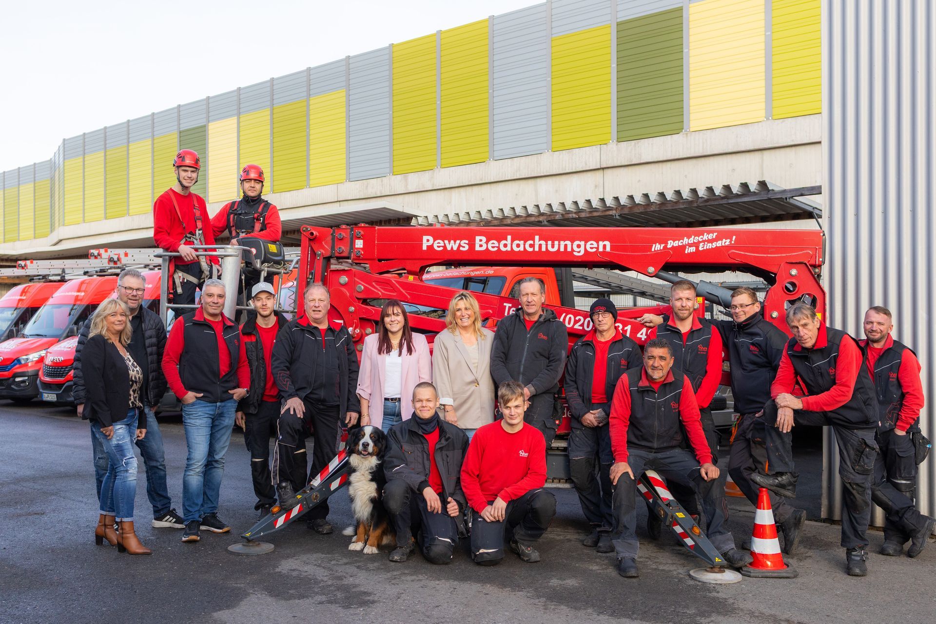 Foto von dem Team | sie stehen vor einem Baufahrzeug | zwei Mitarbeiter stehen auf dem Krahn