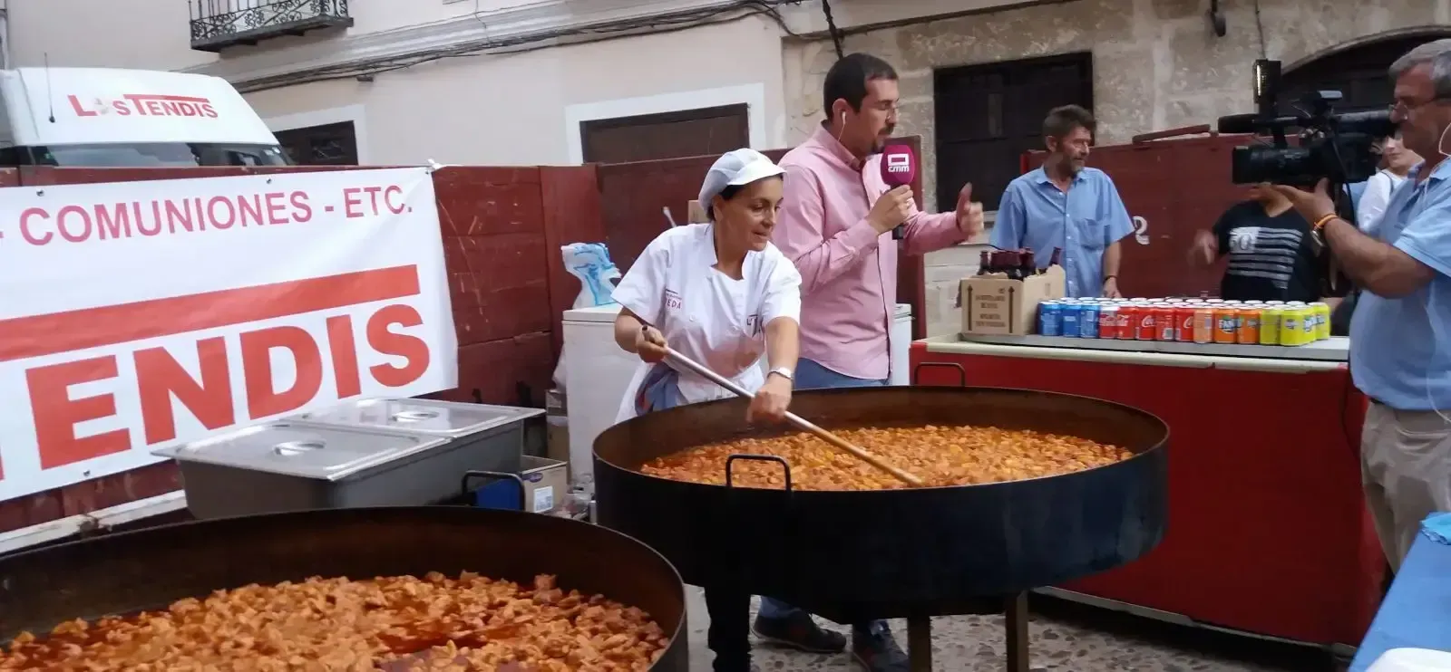 Se está cocinando una gran olla de comida delante de un cartel que dice comuniones, etc.