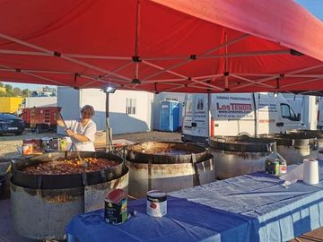 Un hombre está cocinando comida en ollas grandes debajo de una tienda de campaña.